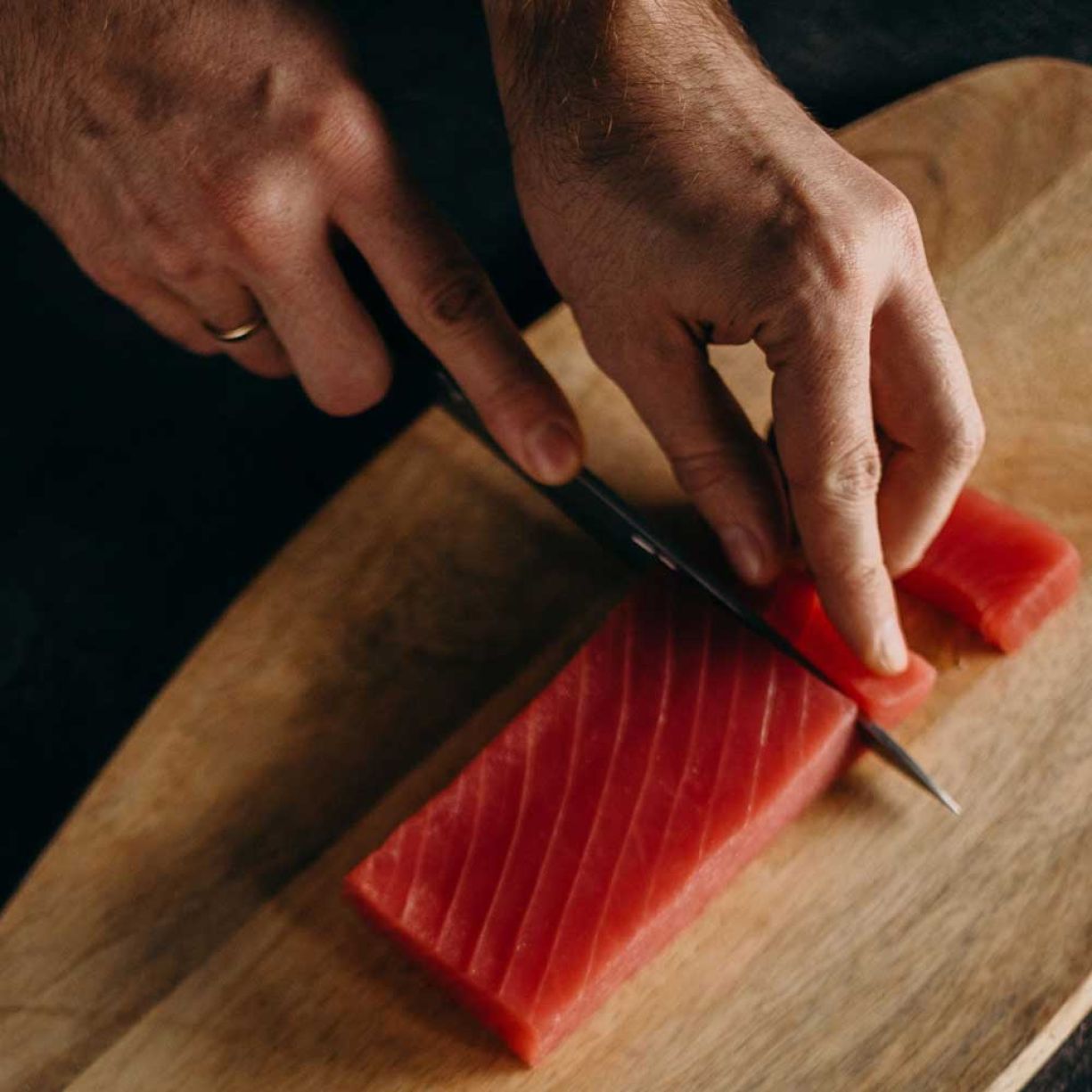 Eine Person verwendet ein Messer, um rohen Thunfisch auf einem Holzbrett zu schneiden.