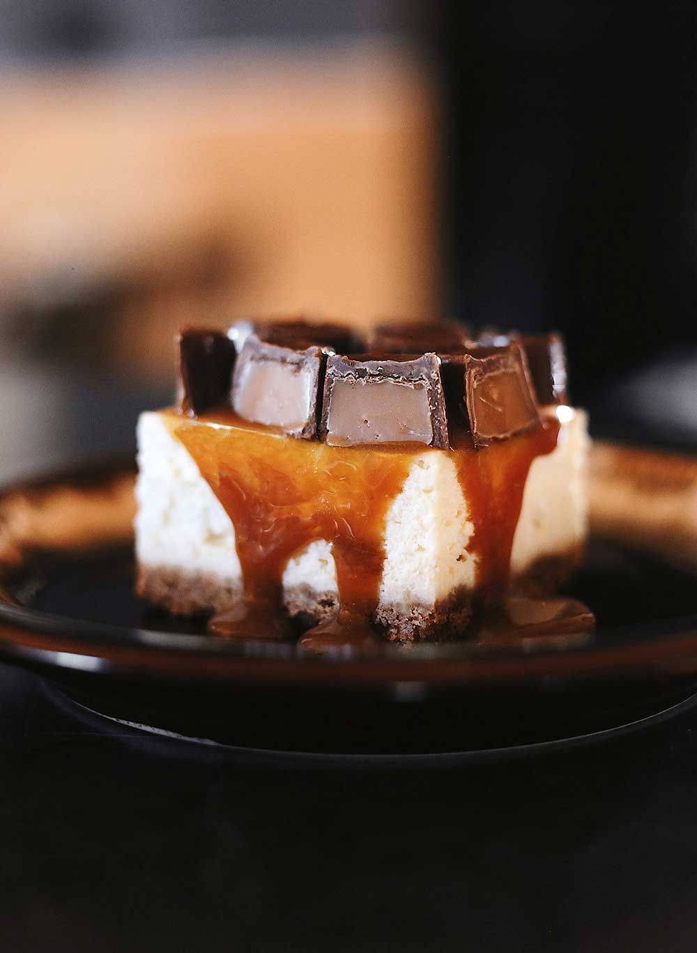 Ein Stück Käsekuchen, garniert mit Karamellsauce, auf einem Teller präsentiert.