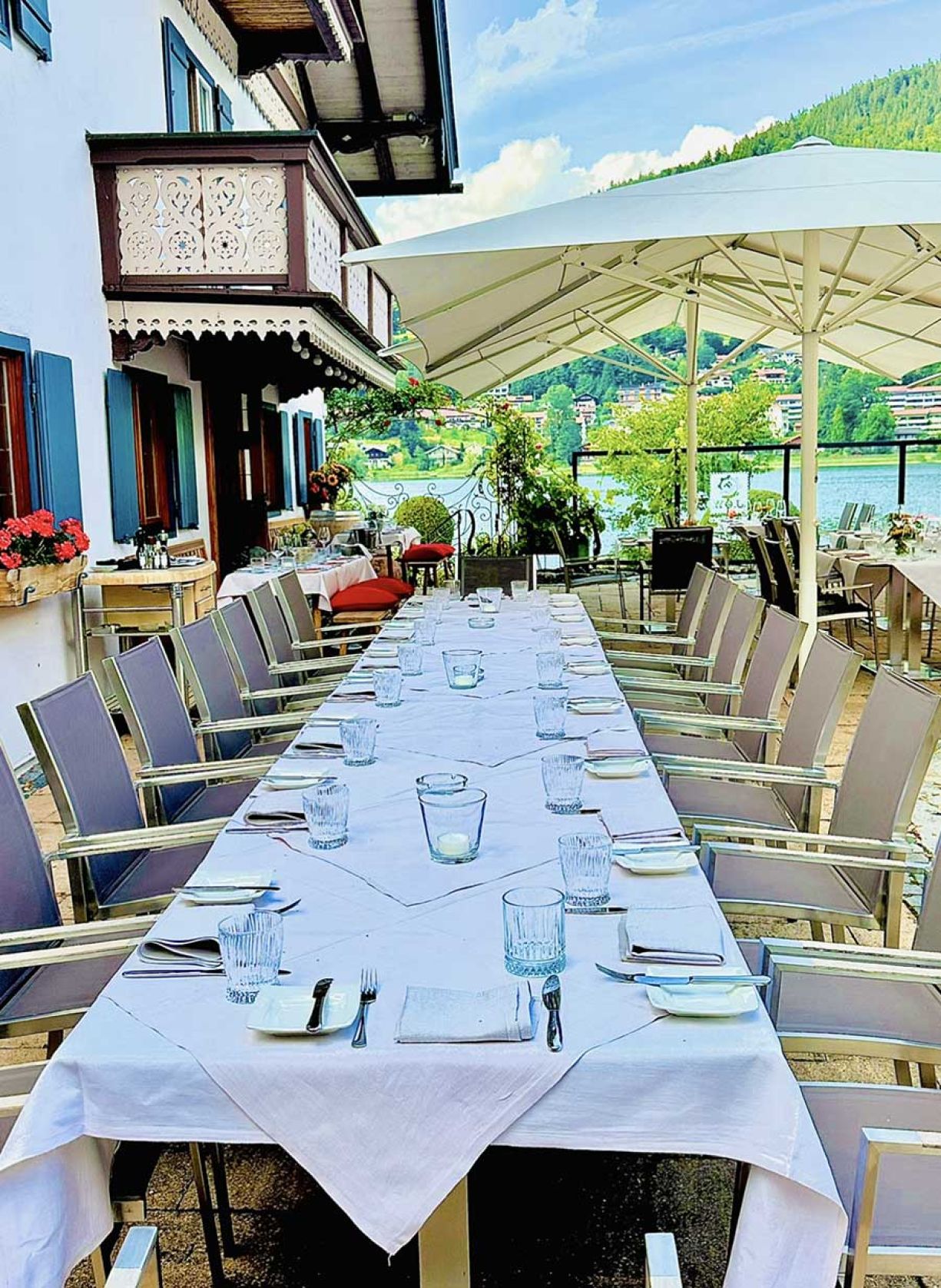 Ein langer Tisch, festlich gedeckt für ein Abendessen auf der Terrasse, umgeben von Pflanzen und sanftem Licht.